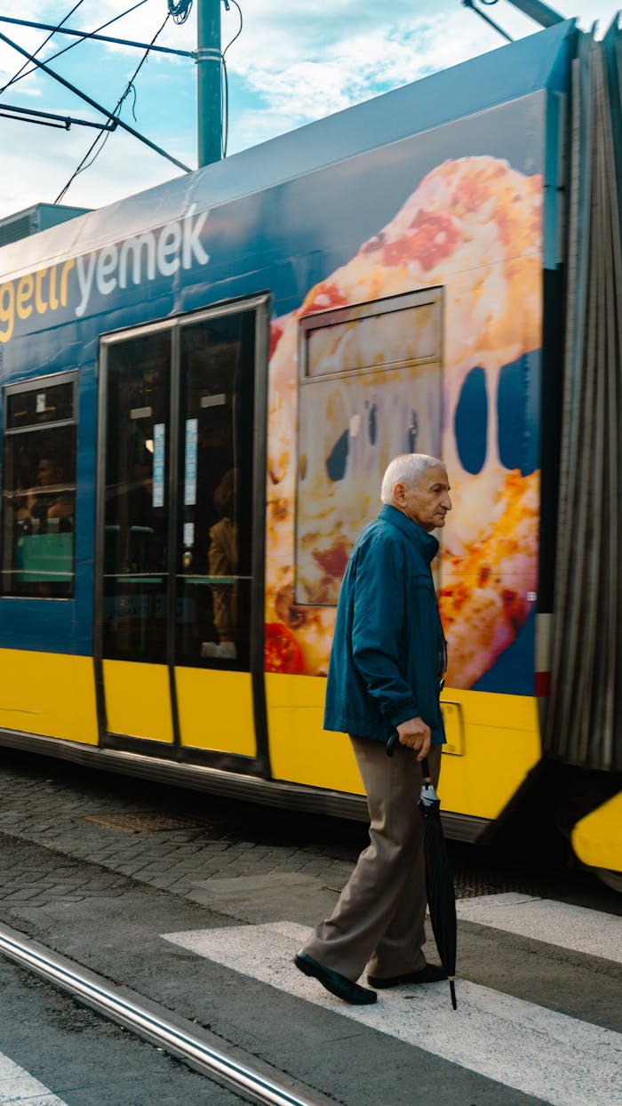 Elderly man crosses street in front of a colorful tram in urban setting.