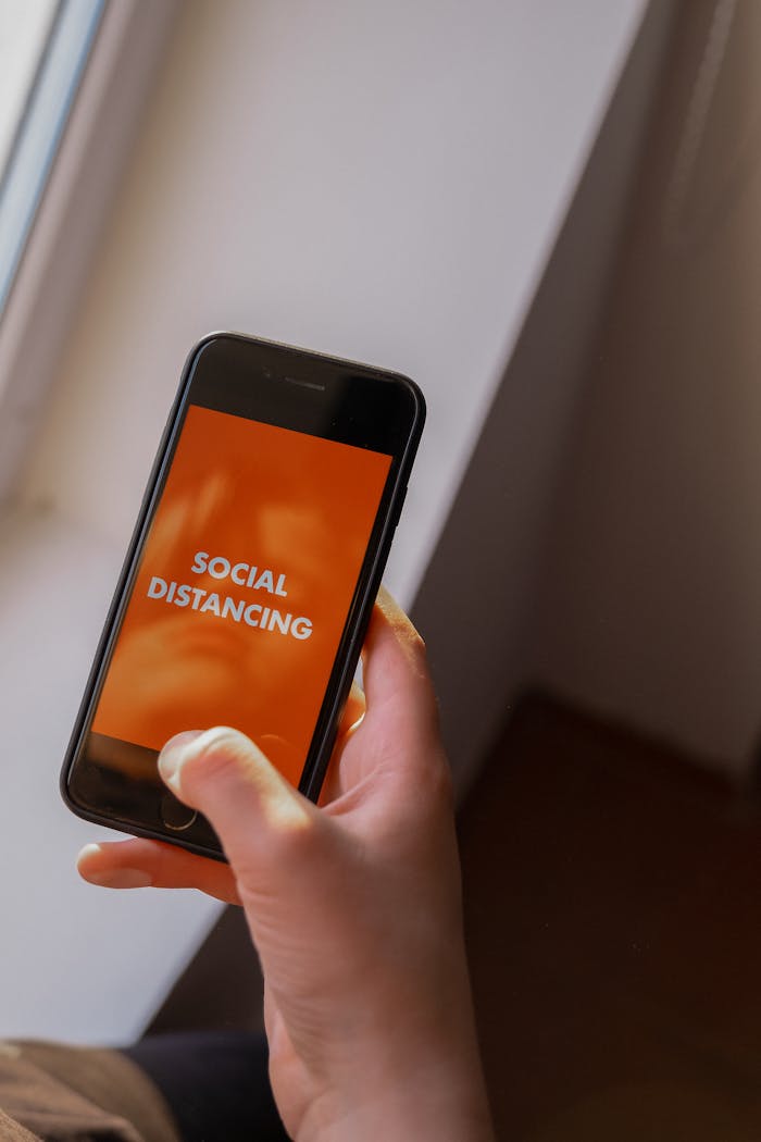 A hand holds a smartphone with a social distancing message on the screen, highlighting pandemic awareness.